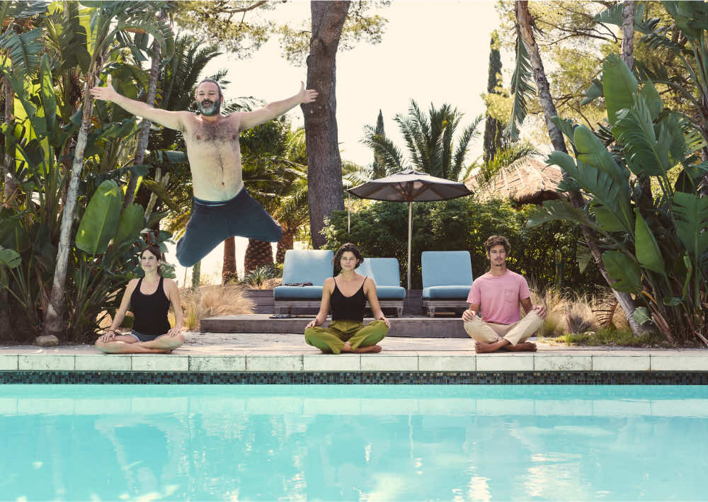 3 people meditating poolside as another man jumps into the pool