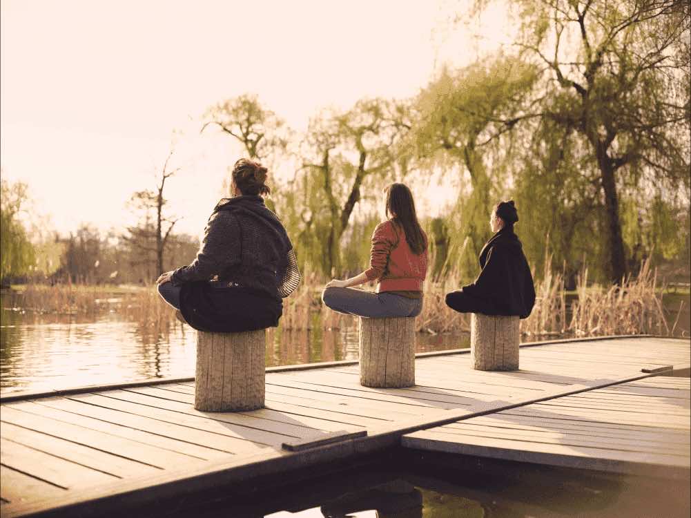 3 women Mindworks members meditating on a dock by a lake
