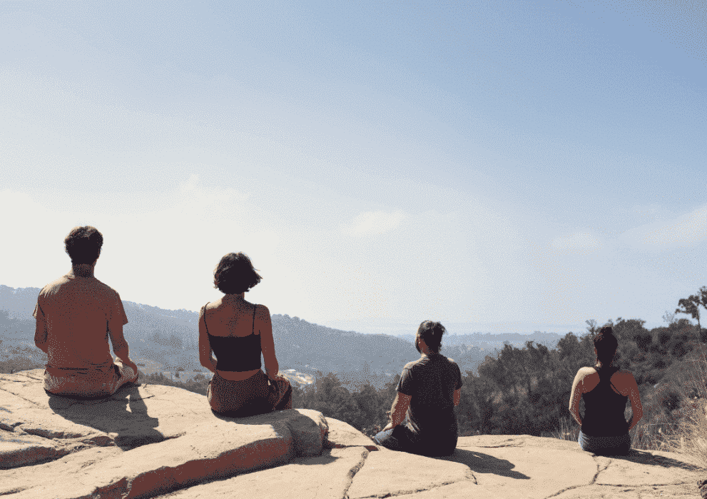 4 friends meditating on a rock overlooking mountains