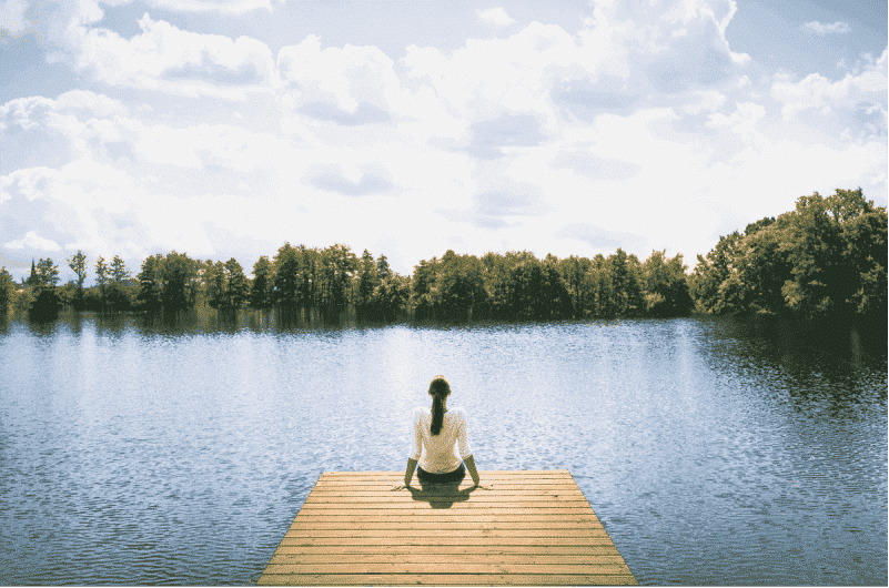 Woman sitting on the end of a dock overlooking a lake while meditating